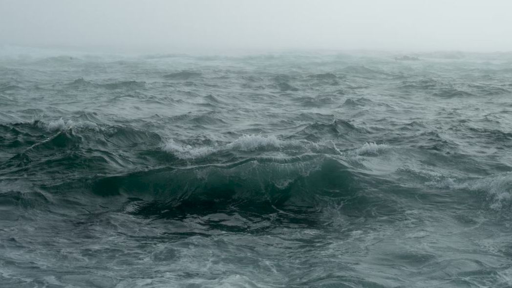The image shows a view of rough ocean waves under a foggy sky, depicting a stormy sea scene.